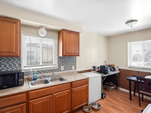 kitchen featuring black microwave, a wainscoted wall, a sink, light countertops, and light wood finished floors