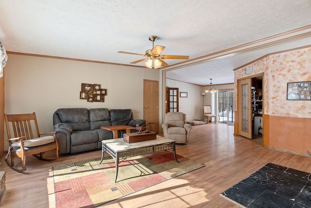 living area with a textured ceiling, ceiling fan with notable chandelier, wood finished floors, and crown molding