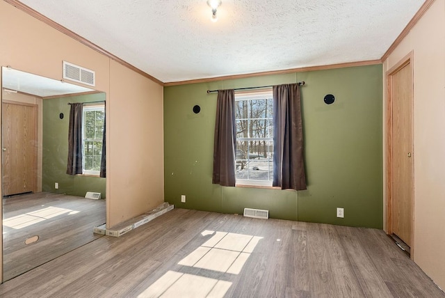 empty room featuring light wood finished floors, plenty of natural light, and visible vents