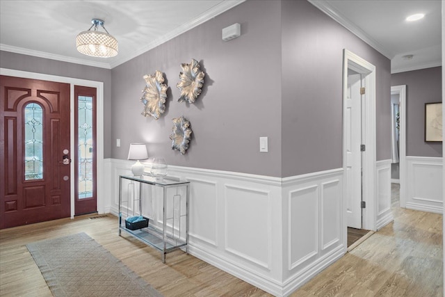 entryway with light wood finished floors, crown molding, and a wainscoted wall