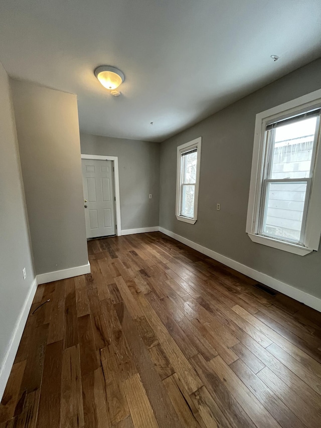 unfurnished room with visible vents, dark wood finished floors, and baseboards