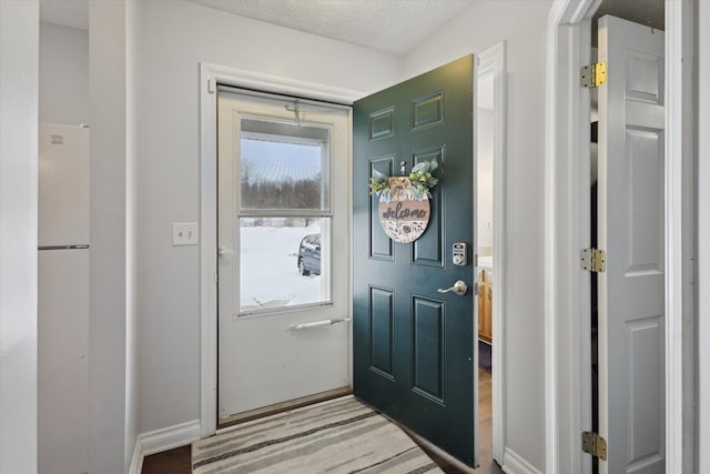 doorway to outside featuring a textured ceiling, baseboards, light wood-style flooring, and a healthy amount of sunlight