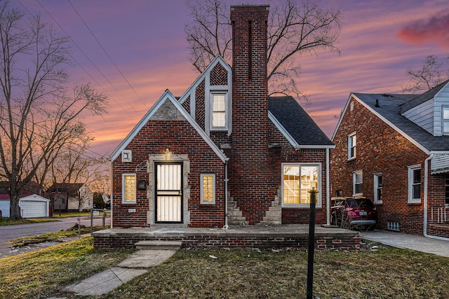 tudor home with brick siding, a lawn, and a chimney