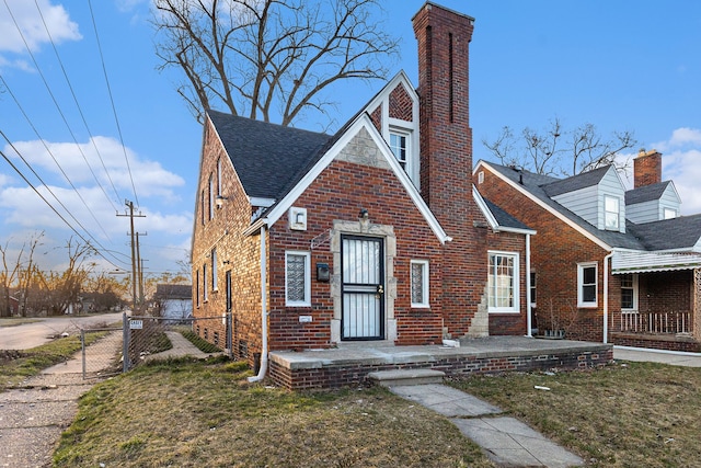 tudor home featuring brick siding, a chimney, fence, and a front yard