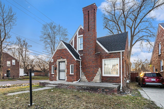 view of front of house with a shingled roof, a chimney, a front lawn, and brick siding