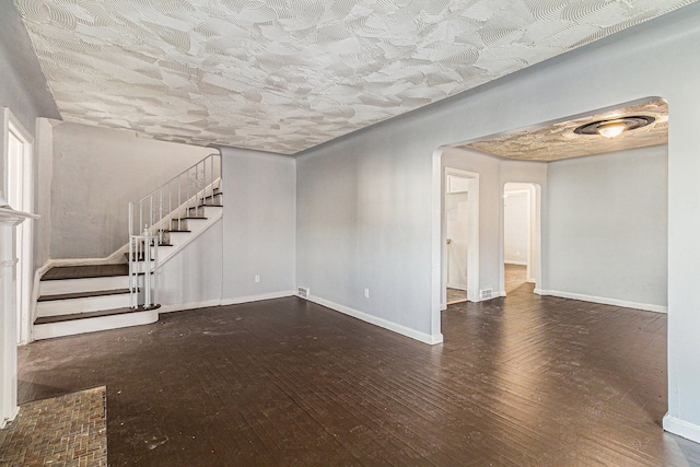 spare room with baseboards, stairway, arched walkways, and dark wood-type flooring