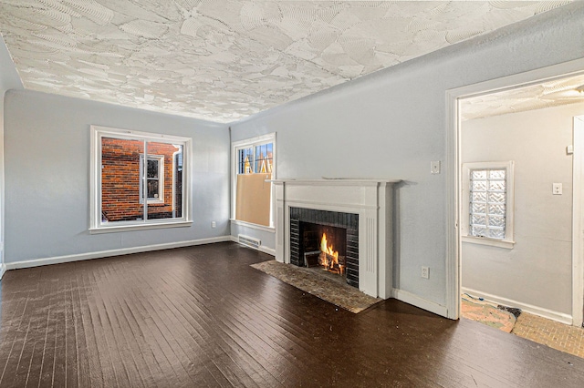 unfurnished living room with dark wood-type flooring, a fireplace with flush hearth, visible vents, and baseboards