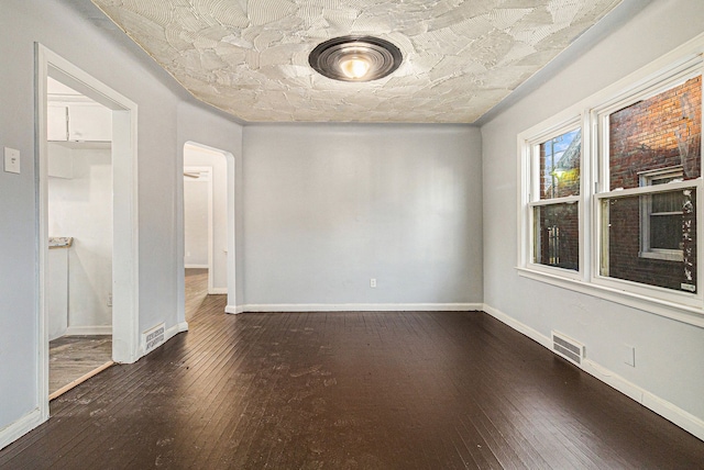 spare room featuring arched walkways, dark wood-style flooring, visible vents, and baseboards