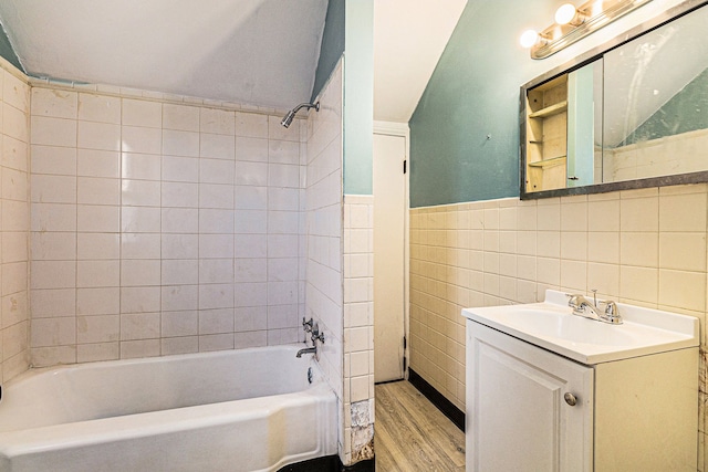 bathroom with a wainscoted wall, shower / tub combination, wood finished floors, vanity, and tile walls