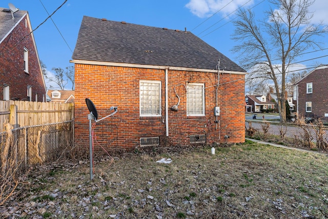 rear view of house featuring a yard, brick siding, a shingled roof, and a fenced backyard