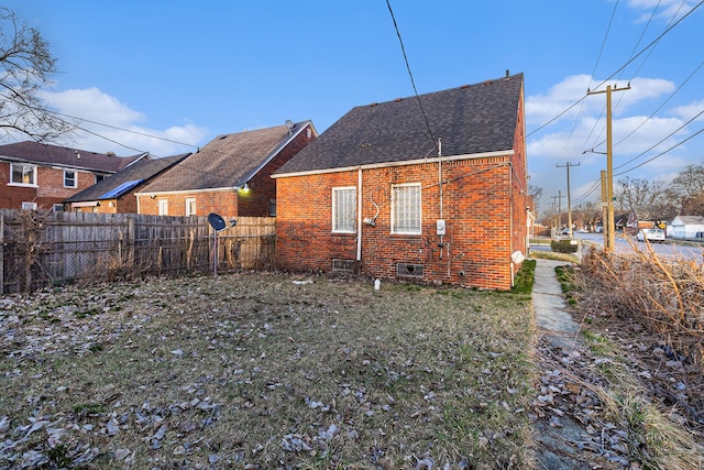 rear view of property featuring brick siding, fence, a lawn, and roof with shingles