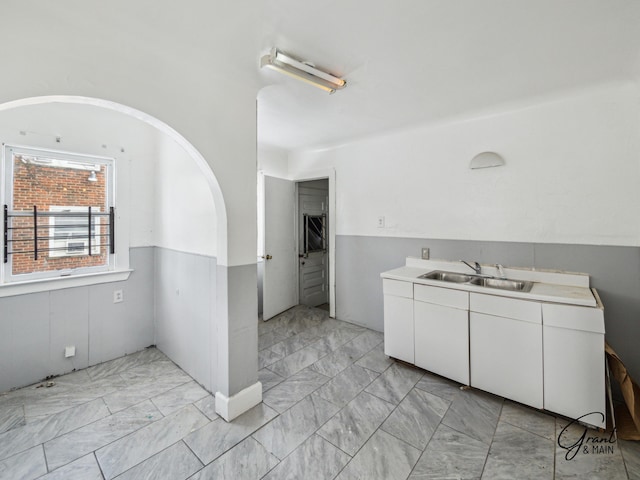 kitchen featuring marble finish floor, white cabinetry, light countertops, and a sink