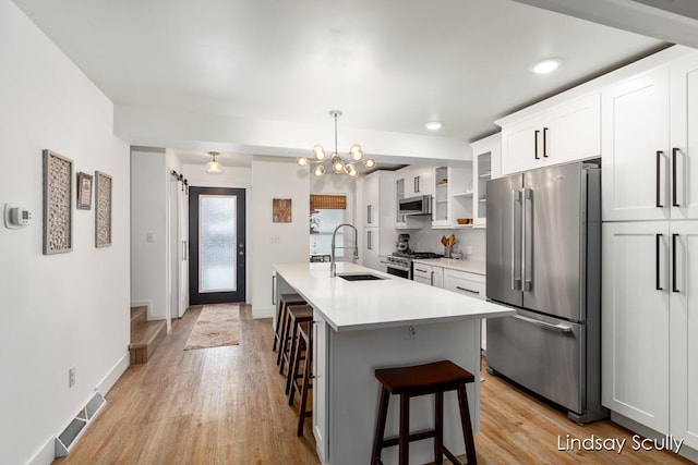 kitchen with stainless steel appliances, light countertops, glass insert cabinets, white cabinetry, and a sink