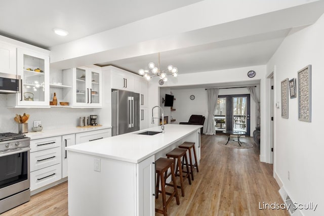 kitchen featuring a kitchen island with sink, stainless steel appliances, light countertops, white cabinetry, and a sink