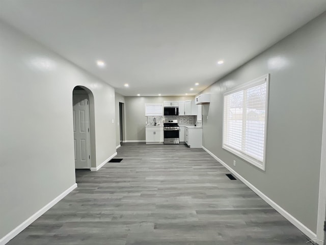 unfurnished living room with light wood finished floors, baseboards, visible vents, arched walkways, and recessed lighting