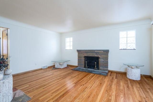 unfurnished living room featuring visible vents, a stone fireplace, baseboards, and wood finished floors