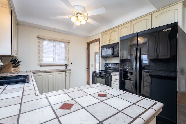 kitchen with tile countertops, ceiling fan, cream cabinets, a sink, and black appliances