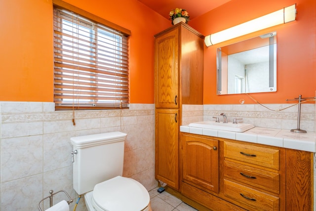 bathroom with a wainscoted wall, tile walls, toilet, vanity, and tile patterned flooring