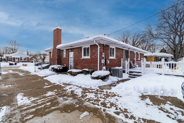 snow covered property featuring a garage, central AC, brick siding, fence, and a chimney