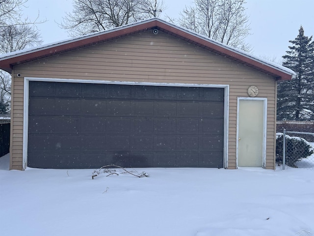 snow covered garage with a detached garage and fence