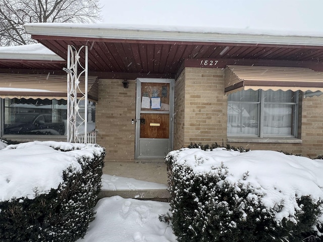 snow covered property entrance featuring brick siding