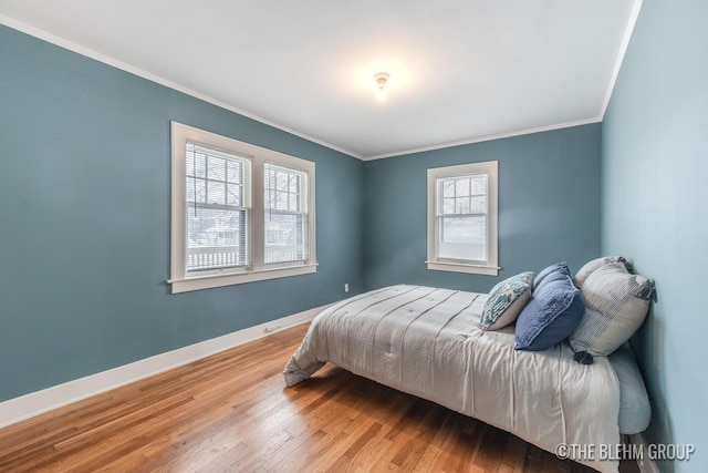 bedroom with ornamental molding, baseboards, and wood finished floors