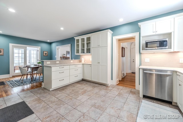 kitchen with appliances with stainless steel finishes, light countertops, glass insert cabinets, and white cabinetry