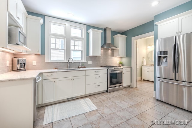 kitchen with wall chimney exhaust hood, appliances with stainless steel finishes, a sink, and white cabinets