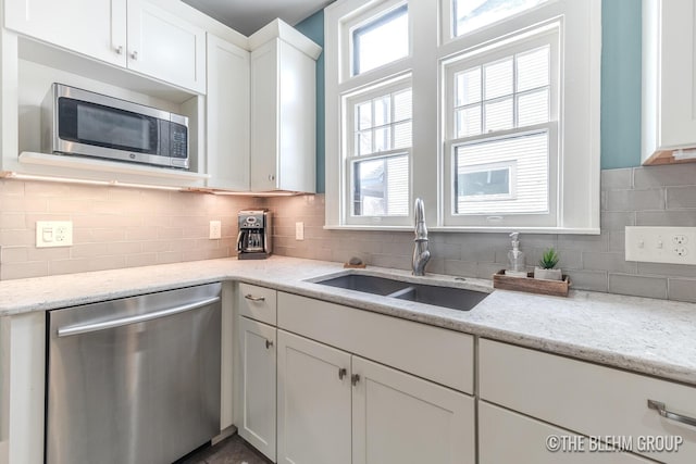 kitchen featuring tasteful backsplash, white cabinets, appliances with stainless steel finishes, light stone countertops, and a sink