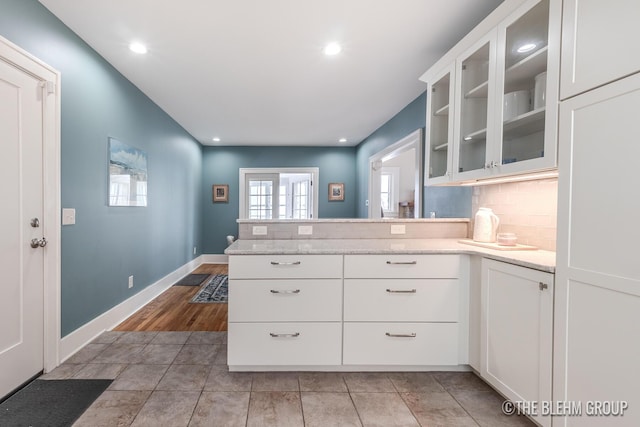 kitchen featuring tasteful backsplash, glass insert cabinets, white cabinetry, a peninsula, and baseboards