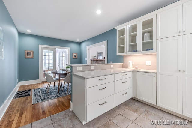 kitchen featuring a peninsula, visible vents, glass insert cabinets, and white cabinets