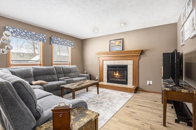 living room featuring light wood finished floors, a fireplace, baseboards, and a textured ceiling