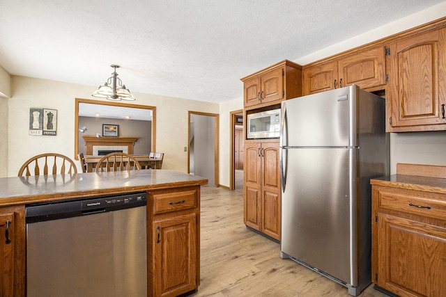 kitchen featuring light wood finished floors, appliances with stainless steel finishes, brown cabinetry, and pendant lighting