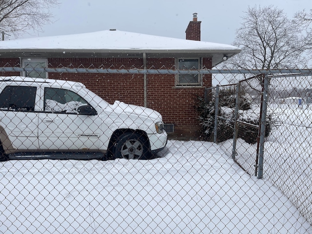 view of snow covered exterior featuring a chimney, fence, and brick siding