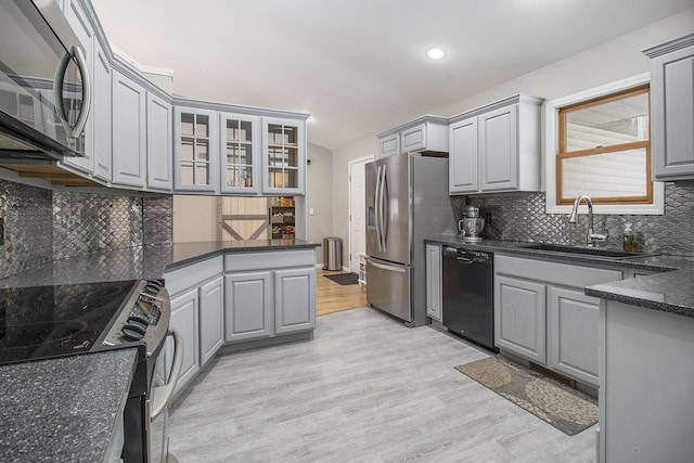 kitchen with gray cabinetry, appliances with stainless steel finishes, light wood-style floors, glass insert cabinets, and a sink