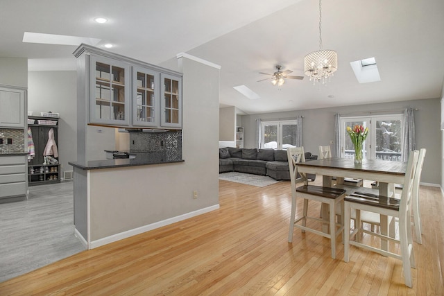 dining room featuring recessed lighting, light wood-style flooring, a chandelier, vaulted ceiling with skylight, and baseboards