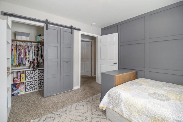 bedroom with a closet, light colored carpet, a decorative wall, and a barn door