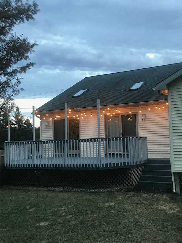 rear view of house featuring a shingled roof, a lawn, and a wooden deck