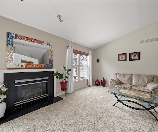 carpeted living room with baseboards, visible vents, vaulted ceiling, and a fireplace with flush hearth