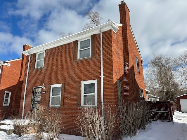 view of snowy exterior featuring brick siding, fence, and a chimney