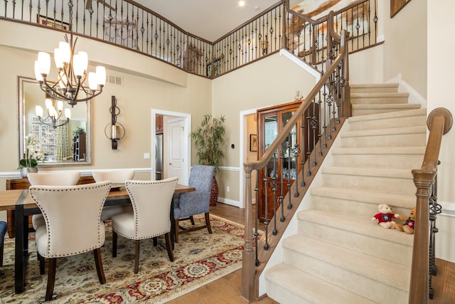 dining room with a chandelier, wood finished floors, a towering ceiling, visible vents, and stairway