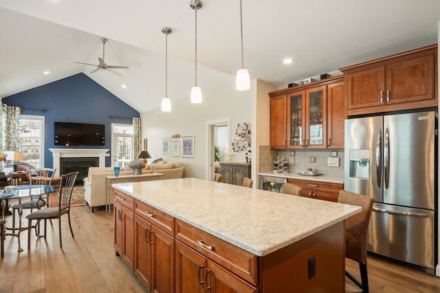 kitchen featuring decorative light fixtures, a kitchen island, open floor plan, stainless steel fridge, and glass insert cabinets