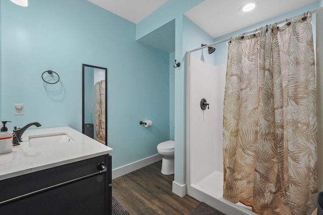 bathroom with toilet, a stall shower, vanity, wood finished floors, and baseboards