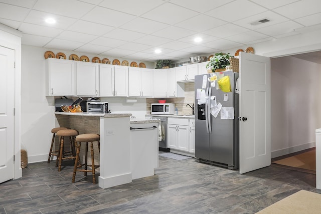 kitchen with a kitchen breakfast bar, white cabinets, stainless steel fridge with ice dispenser, and white microwave