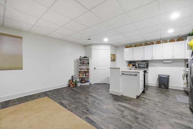 kitchen with white cabinets, a drop ceiling, baseboards, and light stone countertops