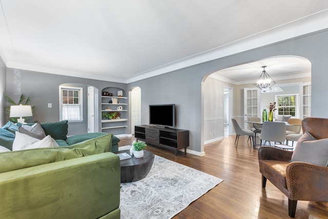 living room with baseboards, wood finished floors, crown molding, built in shelves, and a notable chandelier