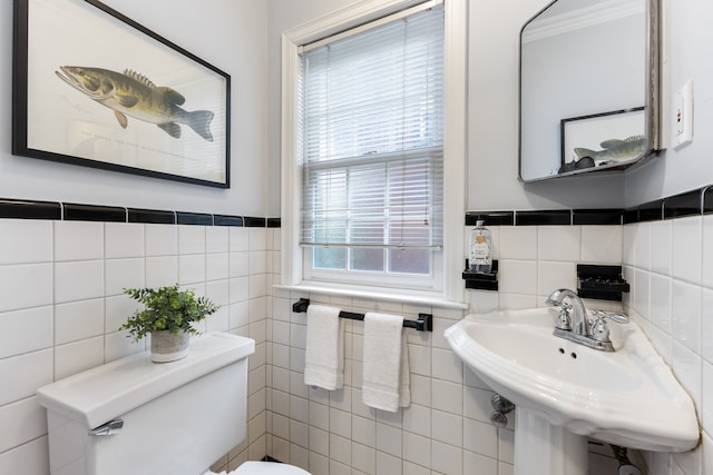 bathroom with toilet, tile walls, a sink, and wainscoting