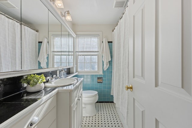 bathroom featuring visible vents, tile walls, toilet, and vanity