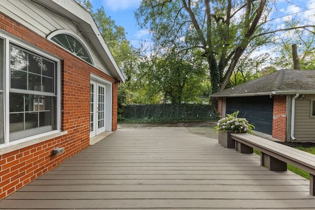 wooden terrace featuring a garage, an outbuilding, and fence