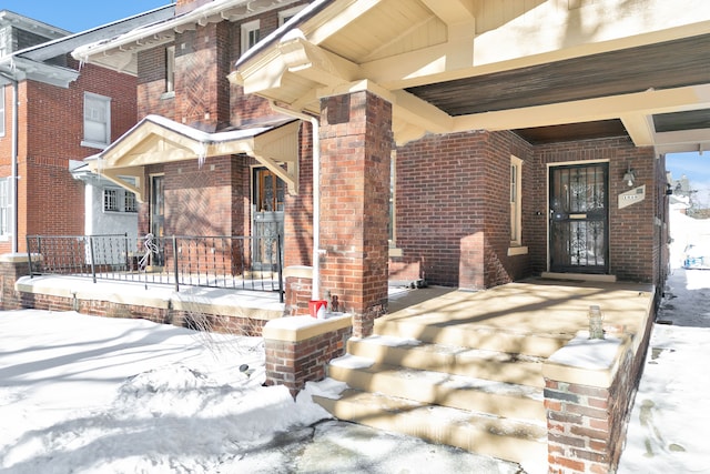 snow covered property entrance featuring covered porch and brick siding